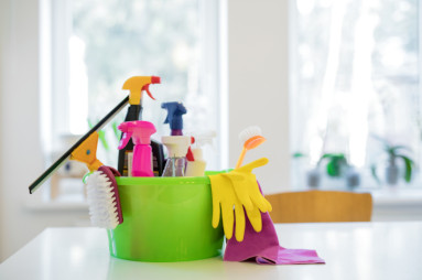 seau de ménage vert avec des produits de nettoyage posé sur une table blanche