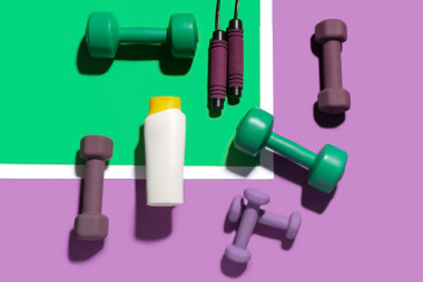 matériel pour un coach sportif qui comporte des altères, une corde à sauter et une gourde situés sur un sol de couleur violet, vert et blanc